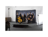 A group of musicians posing with string instruments in a studio setting, with a photographer visible in the foreground and studio lights on both sides.