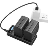 Black battery charger with two batteries attached, plugged into a power outlet on a white background.