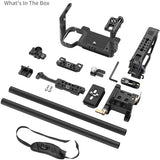 A camera accessory kit laid out on a white background, including a black handle grip, mounting brackets, two carbon-fiber style grip bars, screws, a wrench, and a shoulder strap. Text in the top left reads 'What's In The Box'.