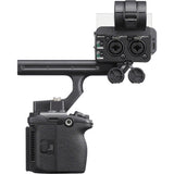 A black camera accessory setup featuring a handheld gimbal handle connected to a camera body, with an additional mounted control module and two small round caps, shown on a plain white background.