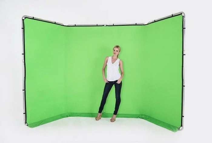 A woman stands in front of a large curved green screen backdrop with a visible black support frame, photographed against a clean white studio background.