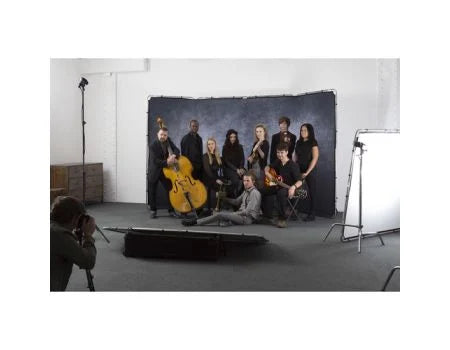 A group of musicians posing with string instruments in a studio setting, with a photographer visible in the foreground and studio lights on both sides.