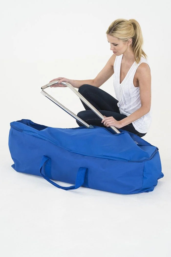 A woman kneels beside a large blue soft-sided storage bag or duffel-style case while holding a metal frame or handle against a clean white studio background.