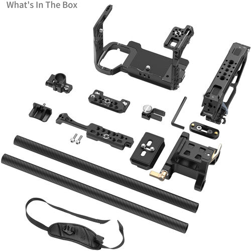 A camera accessory kit laid out on a white background, including a black handle grip, mounting brackets, two carbon-fiber style grip bars, screws, a wrench, and a shoulder strap. Text in the top left reads 'What's In The Box'.