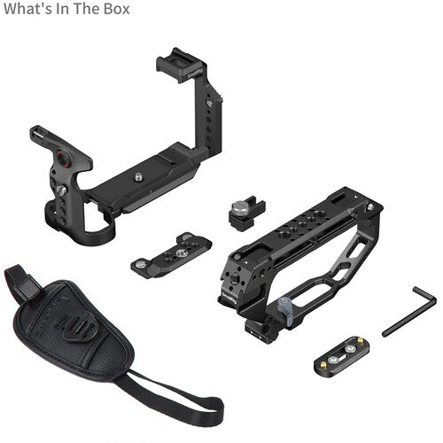 Black camera rig accessory kit laid out on a white background, including a handle grip, mounting brackets, a small Allen wrench, and a strap. Text in the top left reads 'What's In The Box'.