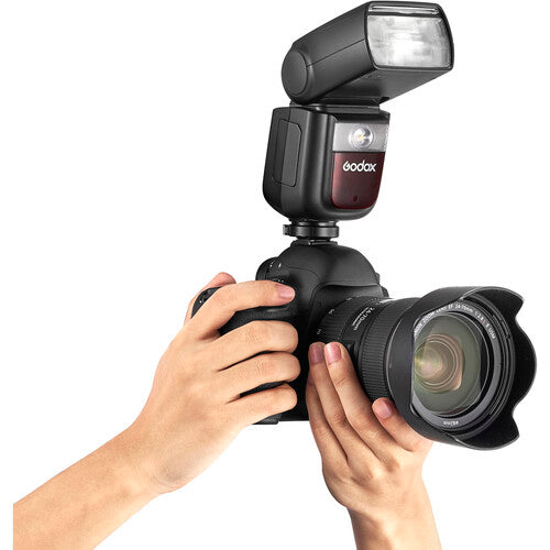 Camera with Godox flash attachment held by a person on a white background