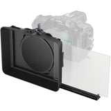A black camera monitor mount with a clear sliding screen panel, shown in front of a faded grayscale camera on a white background.